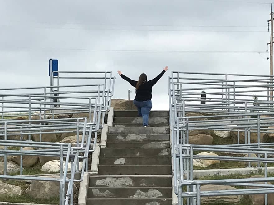 Woman walking up stone steps with arms raised in the air